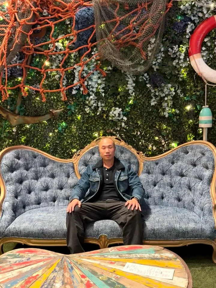 A person sitting on a curved sofa beneath greenery.